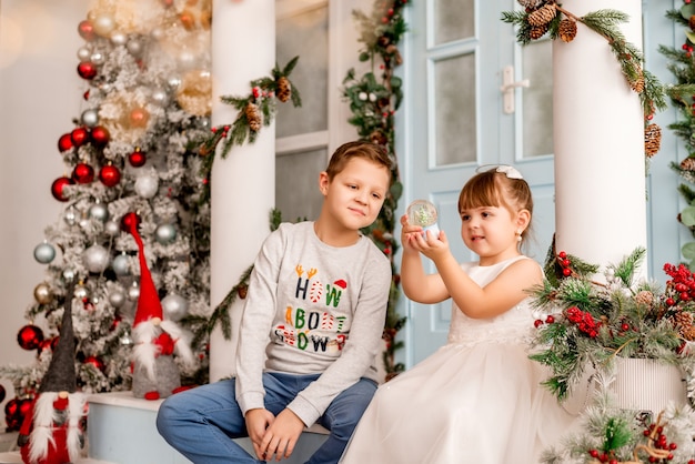 La bambina e suo fratello stanno aprendo i regali di Natale. I bambini vedono un globo di neve a sorpresa