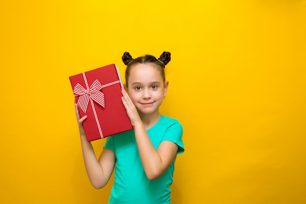 La bambina felice che sta isolata sopra la parete gialla ascolterà sorpresa la scatola, tenendola all'orecchio