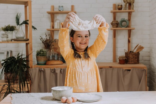 la bambina felice cucina una torta in cucina con un vestito di cotone. Foto di alta qualità
