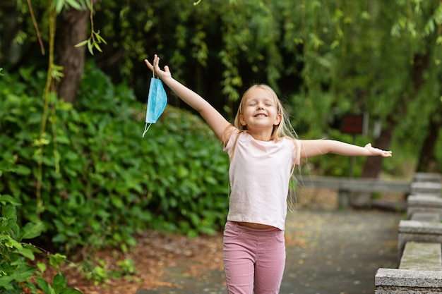 La bambina felice decolla la maschera medica protettiva dal viso all'aperto