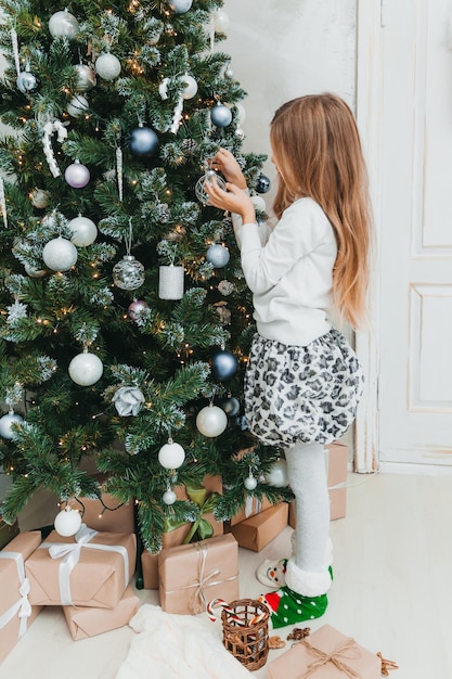 La bambina felice decora l'albero di Natale a casa. vacanze invernali e concetto di persone