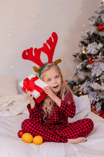 la bambina felice in pigiama a casa si rallegra e disfa i regali per Natale. Foto di alta qualità