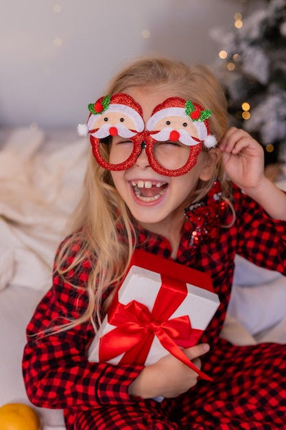 la bambina felice in pigiama a casa si rallegra e disfa i regali per Natale. Foto di alta qualità