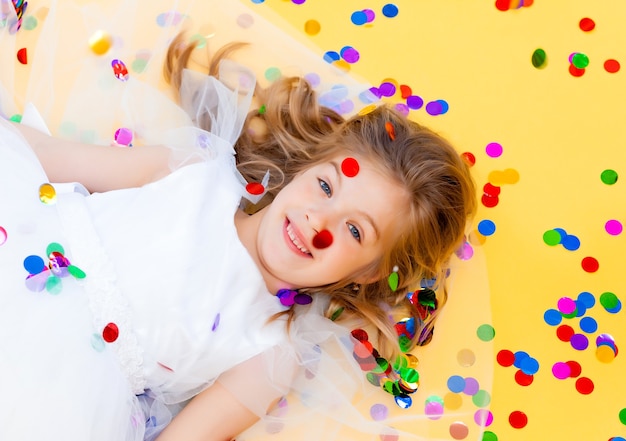 La bambina felice in un vestito bianco celebra una festa con vista dall'alto di coriandoli. Bambino di compleanno, emozioni positive.