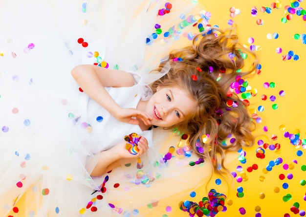 La bambina felice in un vestito bianco celebra una festa con vista dall'alto di coriandoli. Bambino di compleanno, emozioni positive.