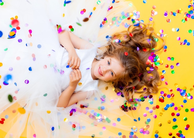 La bambina felice in un vestito bianco celebra una festa con vista dall'alto di coriandoli. Bambino di compleanno, emozioni positive.