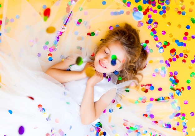 La bambina felice in un vestito bianco celebra una festa con vista dall'alto di coriandoli. Bambino di compleanno, emozioni positive.