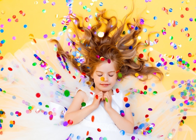 La bambina felice in un vestito bianco celebra una festa con vista dall'alto di coriandoli. Bambino di compleanno, emozioni positive.