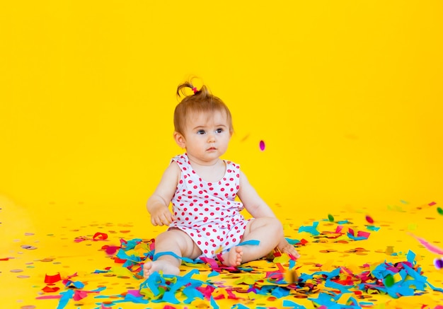 La bambina felice in un vestito in piselli cattura i coriandoli su uno sfondo giallo. posto per il testo