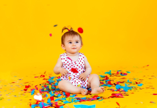 La bambina felice in un vestito in piselli cattura i coriandoli su uno sfondo giallo. posto per il testo