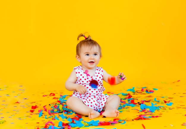 La bambina felice in un vestito in piselli cattura i coriandoli su uno sfondo giallo. posto per il testo