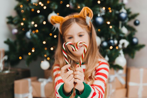 La bambina felice si siede con la caramella vicino all'albero di Natale. Natale.