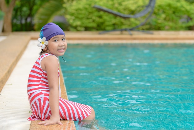 La bambina felice si siede nella piscina all&#39;aperto