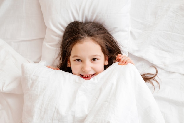 La bambina felice si trova a letto a casa la mattina. sonno sano del bambino. biancheria da letto bianca, spazio per il testo