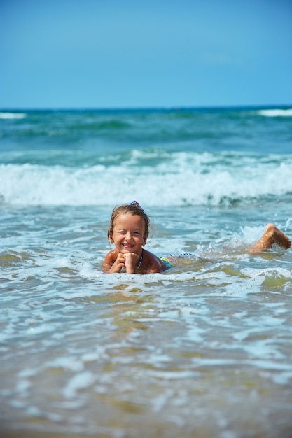 La bambina felice si trova in riva al mare tra le onde durante le vacanze estive sulla spiaggia, il bambino, i bambini giocano al mare, l'estate, le vacanze di ripristino.