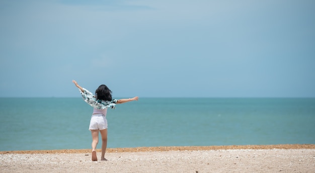 La bambina felice sorride alla grande e alza le braccia sopra la testa con gioia in vacanza in spiaggia sulla riva dell'oceano