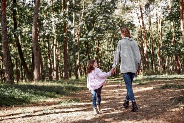 La bambina felice sta camminando con la sua bella madre nella retrovisione della foresta