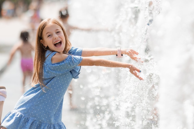 La bambina felice sta giocando nella fontana in una soleggiata giornata estiva