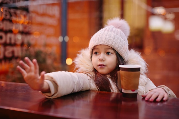 La bambina felice sveglia beve il tè caldo in un caffè della via