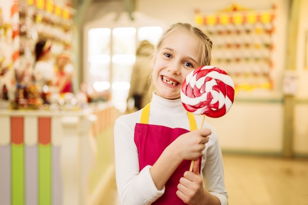 La bambina felice tiene il caramello di zucchero fatto a mano sul bastone. Lecca-lecca fresca nel negozio di caramelle