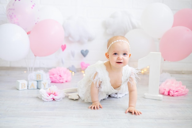 La bambina festeggia il suo primo anno nel giorno del suo compleanno con palloncini rosa sorride e gioisce