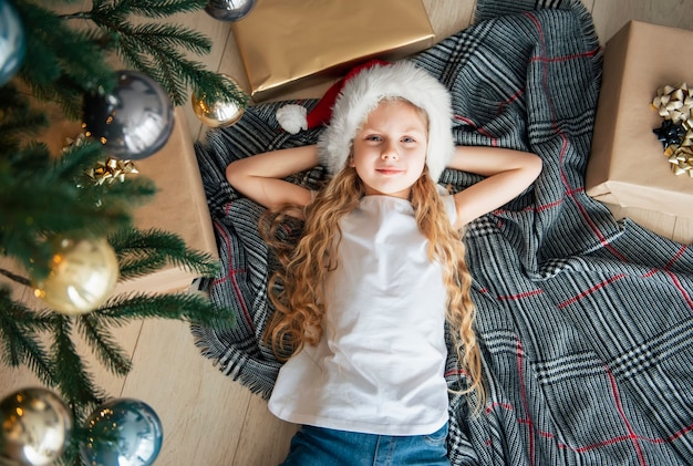 La bambina giace sotto l'albero e sogna. Albero di Natale nell'ampio soggiorno.