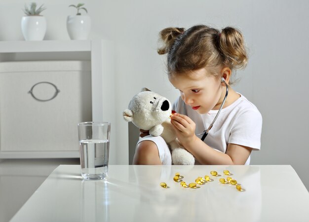 la bambina gioca al dottore nella stanza dei bambini dando capsule gialle a un orsetto