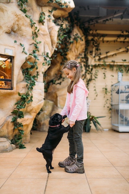 La bambina gioca con il cucciolo divertente nel negozio di animali, amicizia. Bambino con il cane nel negozio di animali, prendersi cura degli animali domestici