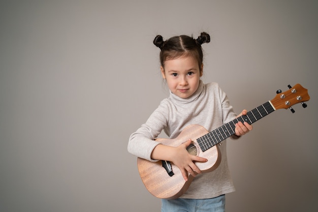 La bambina gioca lo sviluppo creativo dell'ukulele nell'educazione musicale dei bambini fin dall'infanzia insegnando musica online a casa