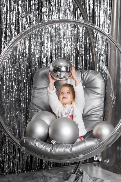 La bambina gioca su una sedia una ciotola di vetro con palline d'argento