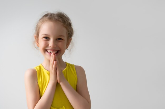 La bambina graziosa è felice di ricevere qualcosa che stava sognando, sorridendo e piegando le mani insieme.