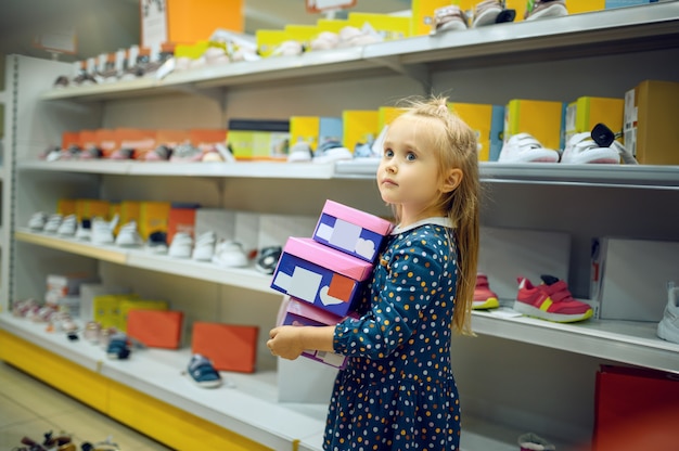 La bambina graziosa tiene la scatola con le scarpe nel negozio per bambini