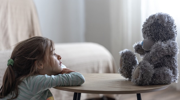 La bambina guarda il suo orsacchiotto, un bambino con un giocattolo preferito su uno spazio di copia di sfondo sfocato.