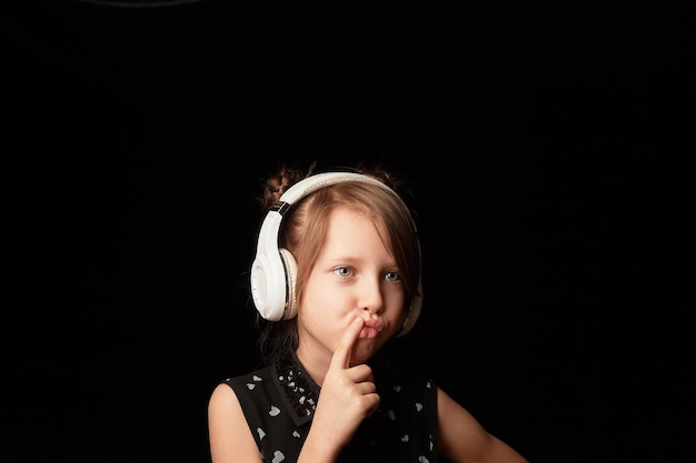 La bambina ha 6 anni Ascolta la musica di racconti audio La difficoltà di scegliere è cosa ascoltare In cuffia wireless bianca su sfondo scuro