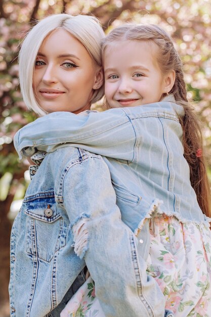 La bambina ha abbracciato sua madre su uno sfondo di sakura in giardino