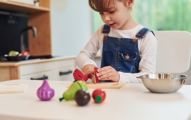 La bambina in abiti casual si siede al tavolo e si diverte giocando con i giocattoli in cucina