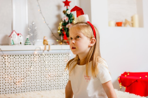 La bambina in cappello della Santa guarda in su e in attesa delle vacanze di Natale