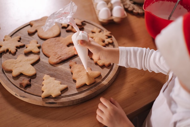 La bambina in cappello di Babbo Natale decora il pan di zenzero usando la glassa bianca tradizioni di natale e capodanno