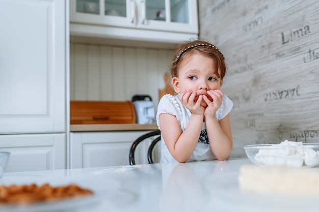 La bambina in cucina è seduta al tavolo ed è annoiata