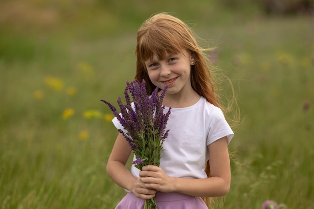 La bambina in maglietta bianca tiene un mazzo di fiori di campo su un prato