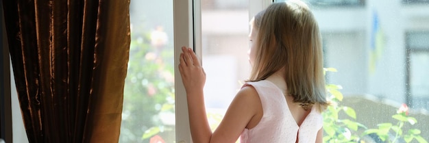 La bambina in piedi alla finestra aperta a casa vista posteriore non lascia i bambini incustoditi concetto