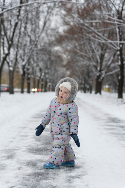 La bambina in tuta sta camminando nel parco innevato.