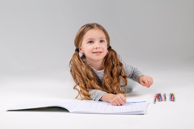 La bambina in un vestito a righe disegna un album sdraiato sullo stile di vita dello sviluppo del bambino del pavimento