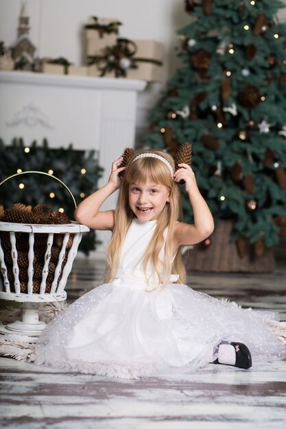 La bambina in un vestito bianco gioca con le pigne nelle decorazioni di Natale