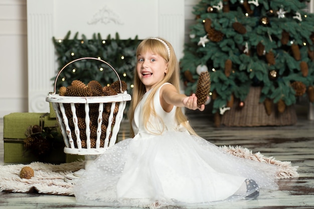 La bambina in un vestito bianco gioca con le pigne