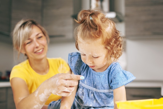 La bambina in un vestito blu, coperto di farina, guarda la mano di sua madre