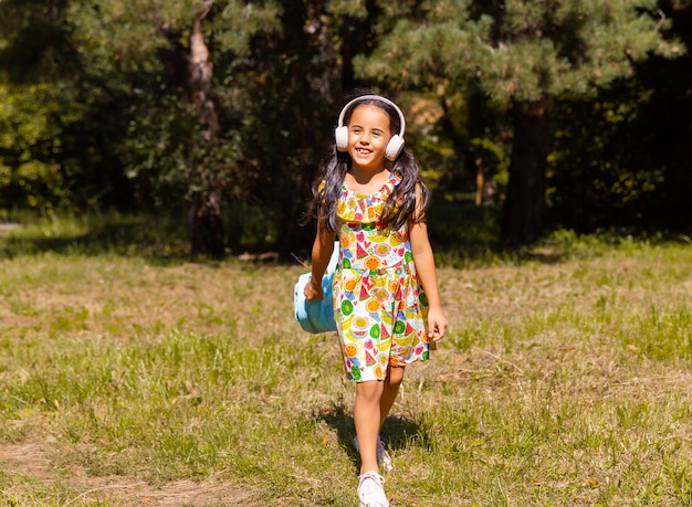 La bambina in un vestito e le cuffie si diverte e salta nel parco sull'erba.