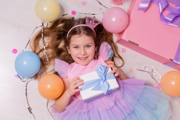 la bambina in un vestito festivo è sdraiata sul pavimento con una confezione regalo nelle sue mani vista dall'alto