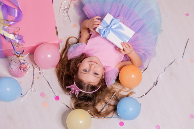 la bambina in un vestito festivo è sdraiata sul pavimento con una confezione regalo nelle sue mani vista dall'alto