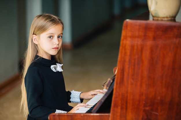 La bambina in un vestito nero impara a suonare il piano. Il bambino suona uno strumento musicale.